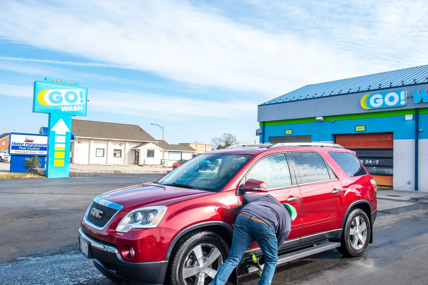 Attendant checking in a red GMC Acadia at GO! Wash Easton II with the sign in the background