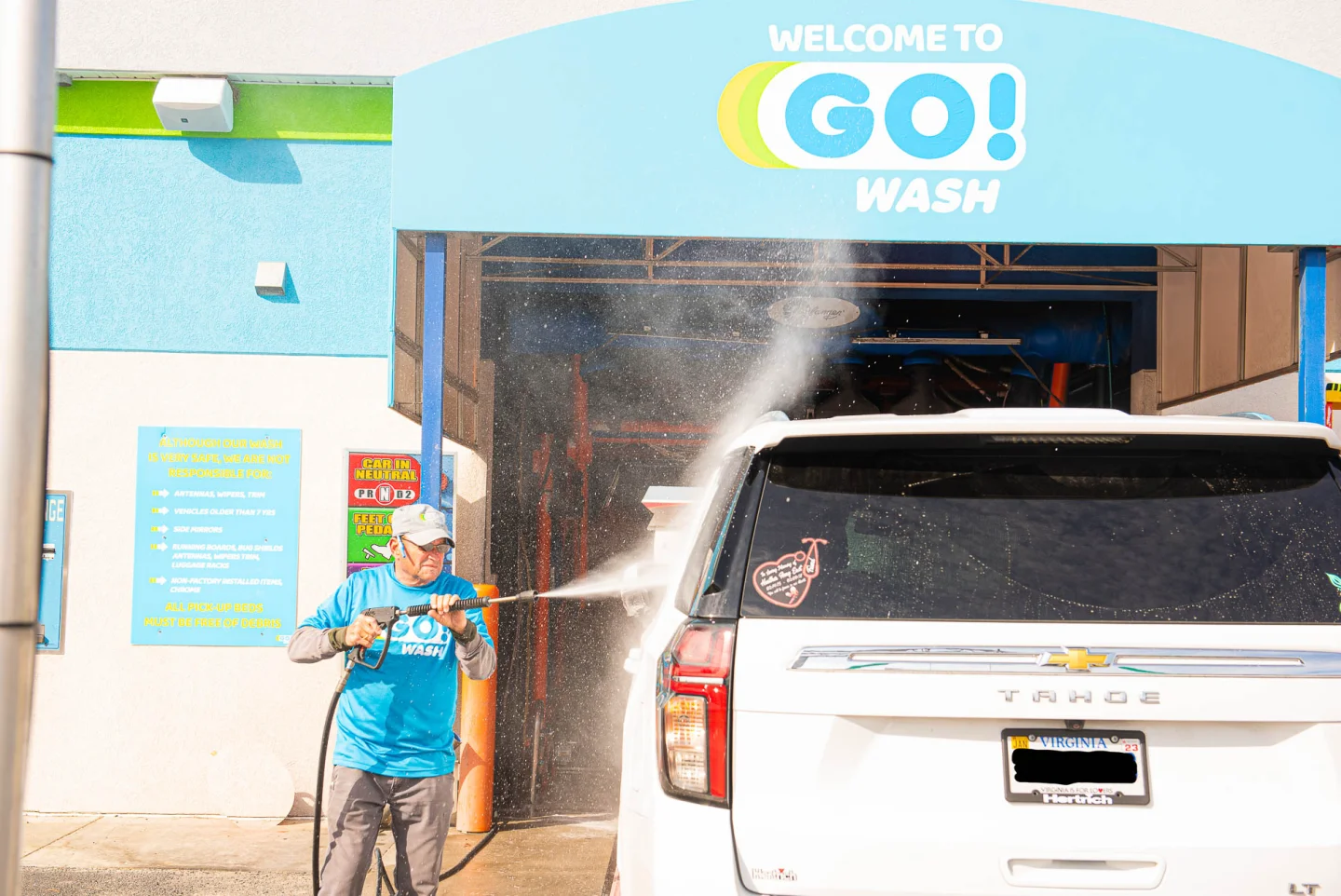 GO! Wash Easton attendant pre-rinsing a white Chevy Tahoe before the tunnel