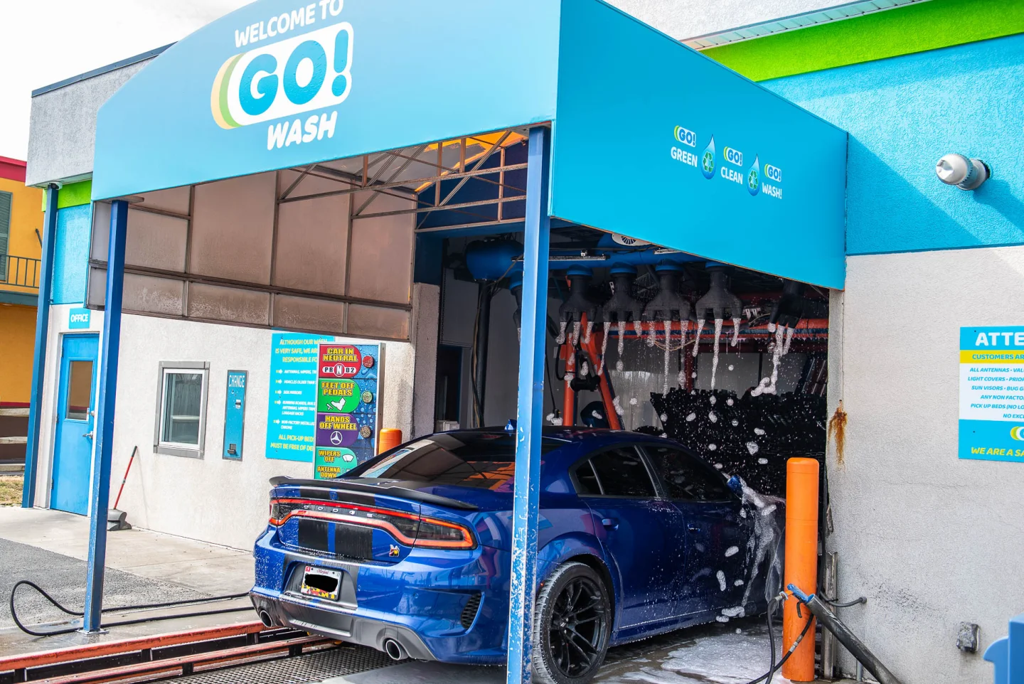 Blue Dodge Charger entering the GO! Wash Easton express tunnel beneath the Welcome sign